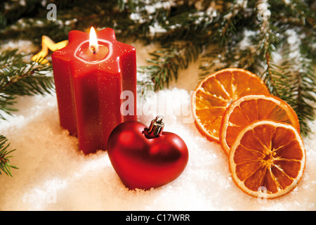Star-shaped candle lit avec un arbre de Noël en forme de cœur, les branches de sapin de Noël, les tranches d'orange séchée et de décorations sur la neige Banque D'Images