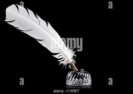 La plume d'une plume blanche et l'encre en cristal bien isolées sur un fond noir. Banque D'Images