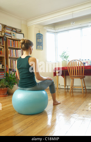 Femme assise sur ballon suisse à la maison Banque D'Images