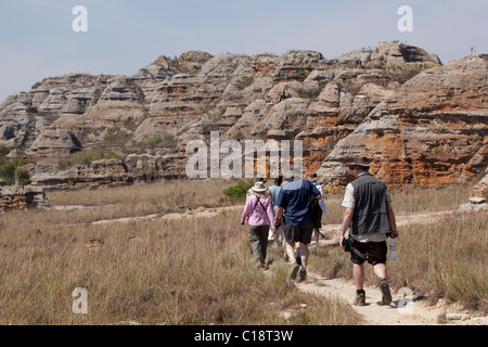 Les touristes de trekking à travers le Parc National d'Isalo, Madagascar, sur fond de falaises de grès érodées du Jurassique. Banque D'Images