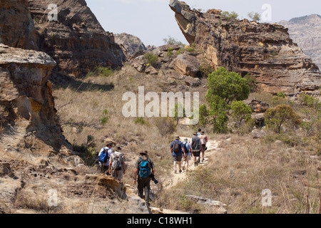 Les touristes de trekking à travers le Parc National d'Isalo, Madagascar, sur fond de falaises de grès jurassique érodé. Banque D'Images