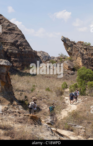 Les touristes de trekking à travers le Parc National d'Isalo, Madagascar, sur fond de falaises de grès jurassique érodé. Banque D'Images