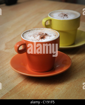 Deux tasses de Cappuccino café dans une orange et jaune mini tasse et soucoupe, avec de la mousse de lait et saupoudrée de chocolat en poudre. Banque D'Images