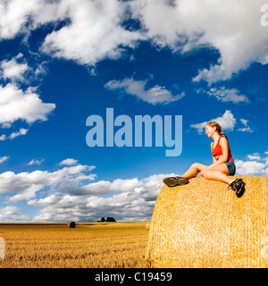 Champ de céréales récoltées, avec une femme assise sur une botte de paille sous les formations de nuages inhabituels dans la luminosité de l'après-midi Banque D'Images