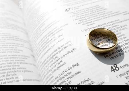 Un anneau de mariage jette une ombre sur les pages ouvertes d'un livre religieux Banque D'Images