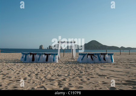 Une plage déserte pour une cérémonie de mariage. Les housses de chaises sont blanches avec des arcs bleu et brun. Une arche attend le couple. Banque D'Images