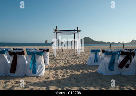 Une plage déserte pour une cérémonie de mariage. Les housses de chaises sont blanches avec des arcs bleu et brun. Une arche attend le couple. Banque D'Images