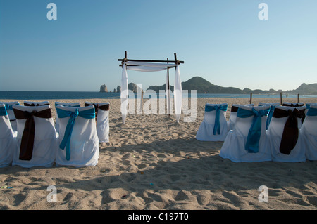 Une plage déserte pour une cérémonie de mariage. Les housses de chaises sont blanches avec des arcs bleu et brun. Une arche attend le couple. Banque D'Images