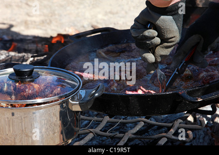 La viande steak des steaks et côtelettes d'agneau mouton la cuisson à feu dans les poêles en fonte sur un feu de camp en plein air. Couper la viande de l'homme. Banque D'Images