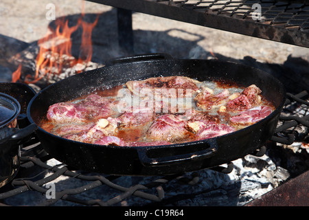 La viande steak des steaks et côtelettes d'agneau mouton la cuisson à feu dans les poêles en fonte sur un feu de camp en plein air. Banque D'Images