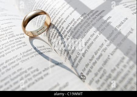 Un anneau de mariage jette une ombre sur les pages ouvertes d'un livre religieux Banque D'Images