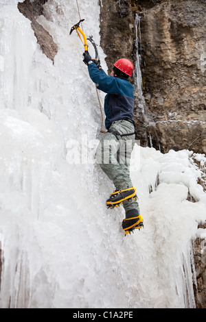 Homme avec piolets et crampons d'escalade sur cascade de glace Banque D'Images