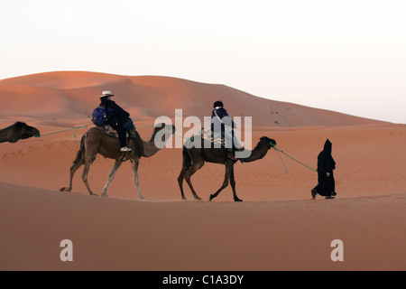 Les touristes sur un voyage de camping de chameau au lever du soleil dans le désert du Sahara, l'Erg Chebbi, Maroc. Banque D'Images