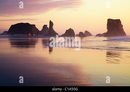 Les touristes de l'équitation sur la plage de l'océan pacifique au coucher du soleil doré, Haystack rocks, nuage réflexions dans le sable humide à marée basse plage de Bandon, Oregon, USA Banque D'Images