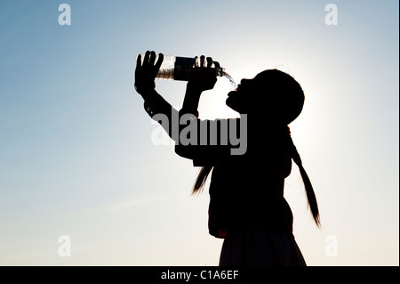 Indian girl boire de l'eau minérale à partir de la bouteille d'eau en plastique. L'Inde. Silhouette Banque D'Images