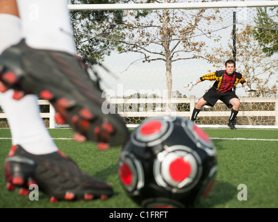 Soccer player kicking ball dans l'objectif sur le terrain de soccer Banque D'Images