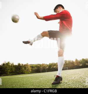 Soccer player kicking ball asiatique sur le terrain de soccer Banque D'Images