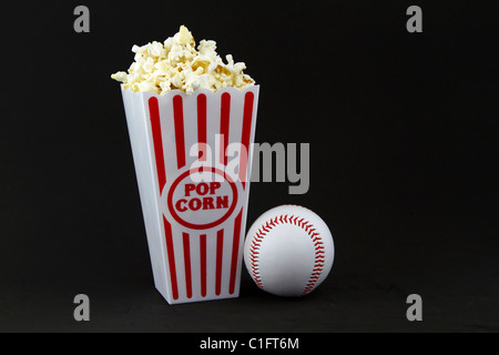 Baseball placé à côté d'un récipient de rouge et blanc frais, chaud, pop-corn, empilées à l'horizontale de l'image. Banque D'Images