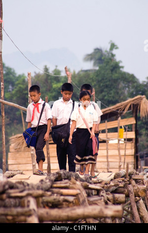 Un groupe de 4 enfants Laotiens sont la marche sur un pied en bois au-dessus d'un pont dans la rivière rural Laos communiste. Banque D'Images