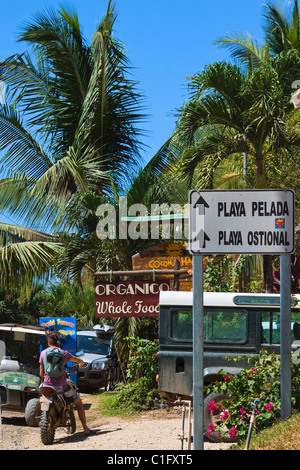 Véhicules, boutiques et signalisation sur la route principale dans le centre de cette zone verte surfer & expatrié communauté, Nosara, Costa Rica Banque D'Images