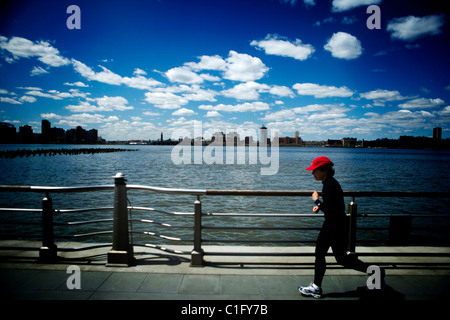 Un runner jogger dans une casquette de baseball rouge avec le ciel de New York en arrière-plan le long de la rivière Hudson. Banque D'Images