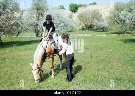 Dame équitation sur le cheval avec son entraîneur à l'extérieur. La lumière naturelle et les couleurs Banque D'Images