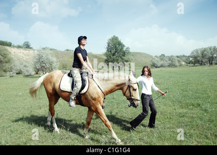 Dame équitation sur le cheval avec son entraîneur à l'extérieur. La lumière naturelle et les couleurs Banque D'Images