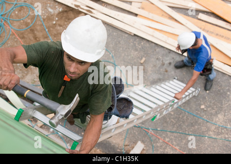 Les charpentiers sur une longue échelle pour l'installation sur un site de construction revêtement Banque D'Images