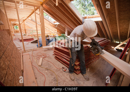 Carpenter en utilisant une scie circulaire sur le toit à chevrons d'une maison en construction Banque D'Images