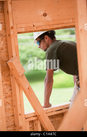Hispanic carpenter à partir de la fenêtre Ouverture de deuxième étage à une maison en construction Banque D'Images