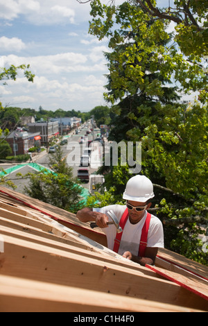 Hispanic carpenter hammering sur fenêtre de toit ouvrant sur une maison en construction Banque D'Images