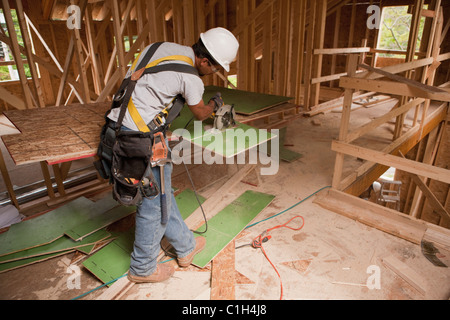 Carpenter en utilisant une scie circulaire sur le revêtement mural extérieur dans une maison en construction Banque D'Images