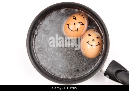 Deux œufs durs avec des visages heureux l'ébullition dans une casserole. Banque D'Images