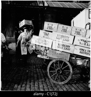 1950s, un porteur en salopette sale déplaçant des caisses d'un chariot en bois de Hine Bros d'Aberdeen, au Smithfield Wholesale Meat Market, Londres, Angleterre. Banque D'Images