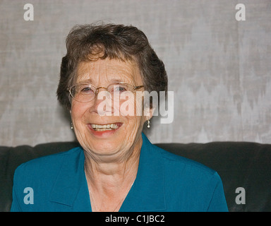 Cette femme âgée est souriant et heureux et portant une chemise de couleur turquoise. Elle a des lunettes et cheveux grisonnants courts. Banque D'Images