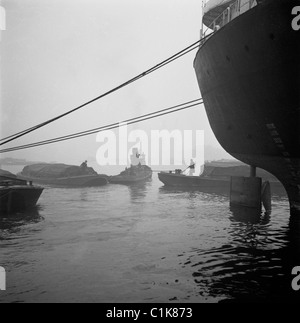 Londres, années 1950. Une photographie par J Allan l'argent comptant. Le brouillard entoure un remorqueur comme il moors à Londres Dock. Banque D'Images