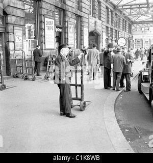 Londres, années 1950. Une photographie de J Allan Cash d'un porteur de chemin de fer âgé sur le pavé à l'extérieur de la gare de Victoria alors qu'il attend un client. Banque D'Images