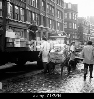 Années 1950, dans une rue pavée humide, des porteurs déchargent du poisson d'un camion sur des charrettes au célèbre marché aux poissons Billingsgate à Lower Thames St, Londres. Banque D'Images