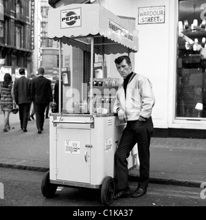 1960s, Londres. Stand portable pour hot dogs et vendeur masculin au coin de Wardour Street, dans cette photo historique de J Allan Cash. Banque D'Images