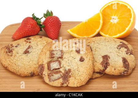 Cookies aux pépites de chocolat disposés sur une planche en bois et décoré avec des fraises et des oranges. Fond blanc - close-up Banque D'Images