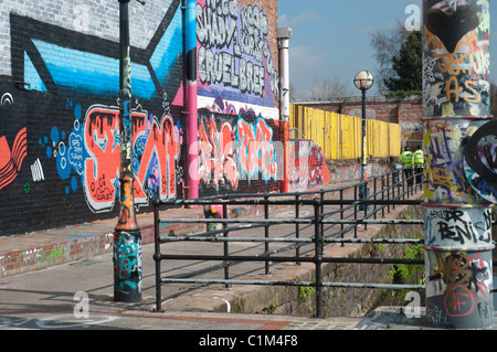 Des murs couverts de graffitis et du mobilier urbain sur les rives de la rivière Irwell, Salford.au loin deux policiers en patrouille. Banque D'Images