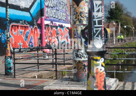 Des murs couverts de graffitis et du mobilier urbain sur les rives de la rivière Irwell, Salford.au loin deux policiers en patrouille. Banque D'Images