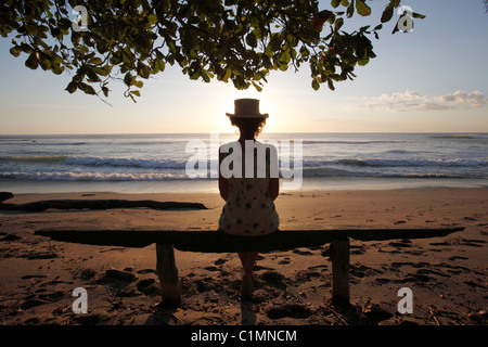 Une femme assise sur un banc à regarder le coucher du soleil sur la Playa Avellanas, Péninsule de Nicoya, Costa Rica Banque D'Images