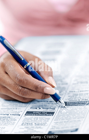 Main de femme noire entourant votre annonce dans le journal section classifiée à job Banque D'Images