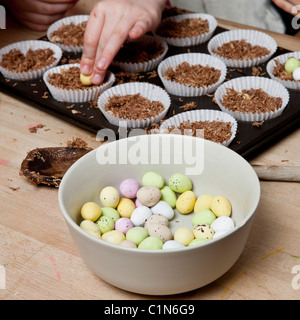 Les enfants faire de nid de Pâques cupcakes faits avec du blé filamenté, sirop, chocolat et sucre au chocolat enrobés de mini-oeufs. Banque D'Images