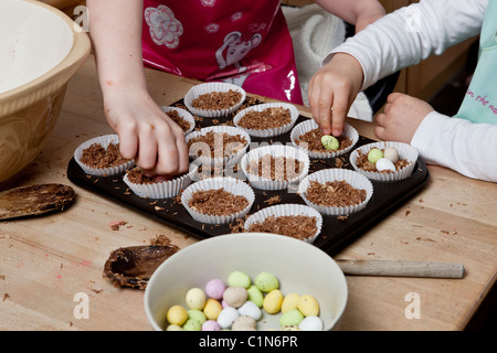 Les enfants faire de nid de Pâques cupcakes faits avec du blé filamenté, sirop, chocolat et sucre au chocolat enrobés de mini-oeufs. Banque D'Images