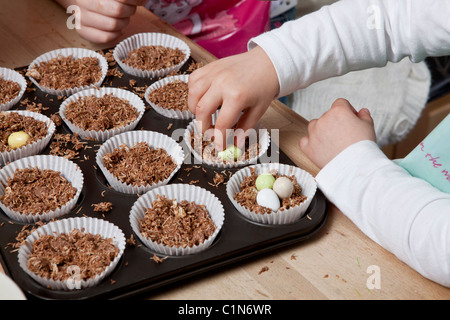 Les enfants faire de nid de Pâques cupcakes faits avec du blé filamenté, sirop, chocolat et sucre au chocolat enrobés de mini-oeufs. Banque D'Images