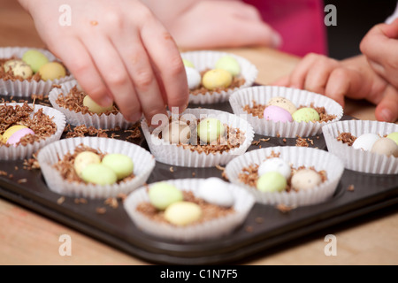 Les enfants faire de nid de Pâques les gâteaux avec shredded wheat et mini oeufs en chocolat. Banque D'Images