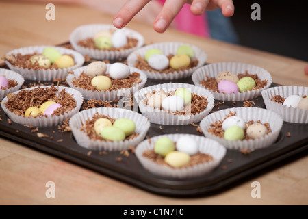 Les enfants faire de nid de Pâques cupcakes avec shredded wheat et mini des œufs en chocolat / Chocolat Mini-oeufs. Banque D'Images