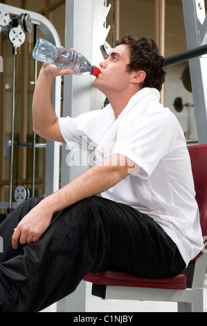 Homme portant un t-shirt blanc de l'eau potable sur une machine d'exercice à la salle de sport Banque D'Images